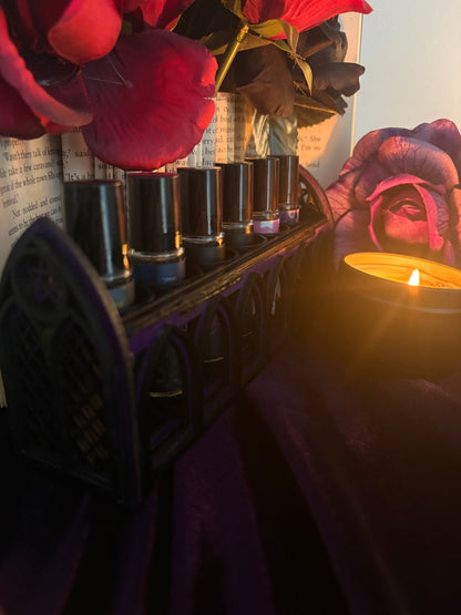 A set of six black cosmetic tubes arranged in a dark decorative tray, styled with red flowers and a lit candle in warm, moody lighting.